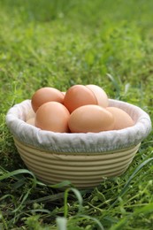 Photo of Fresh chicken eggs in basket on green grass outdoors