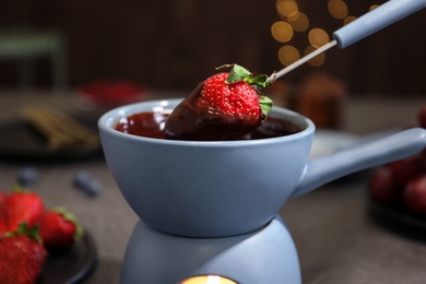 Photo of Dipping strawberry into pot with chocolate fondue on table, closeup