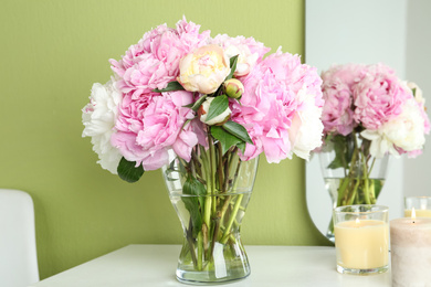 Photo of Beautiful peonies and candles on white dressing table near green wall