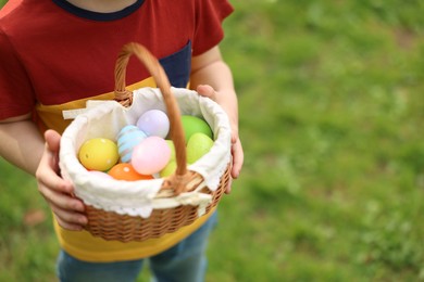 Photo of Easter celebration. Little boy holding basket with painted eggs outdoors, closeup. Space for text