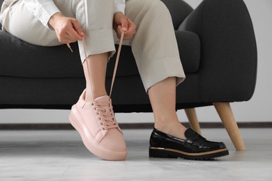 Photo of Woman taking off uncomfortable shoes and putting on sneakers in office, closeup