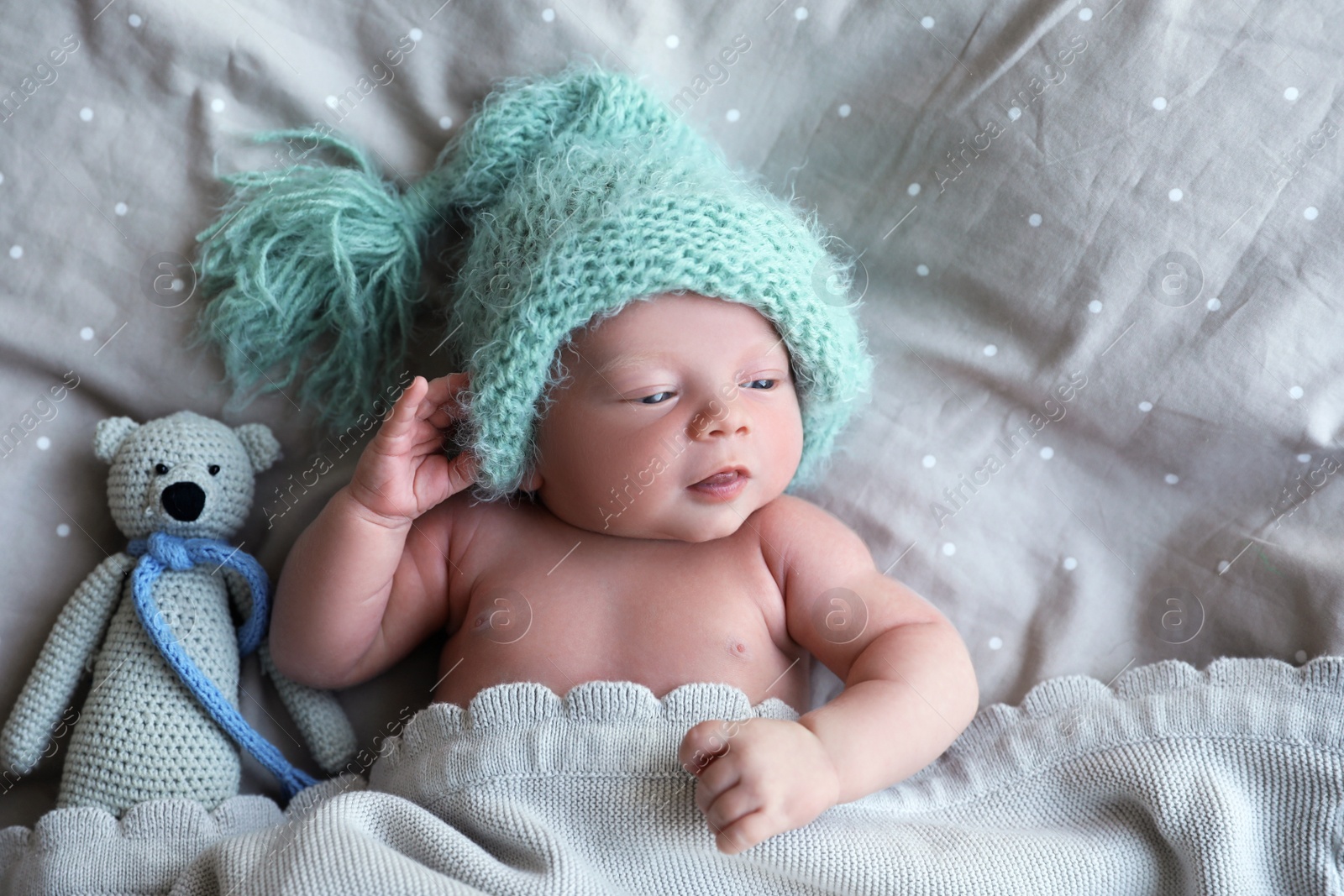 Photo of Cute newborn baby in warm hat with toy lying on bed, top view