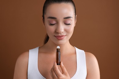 Beautiful young woman with bottle of essential oil on brown background