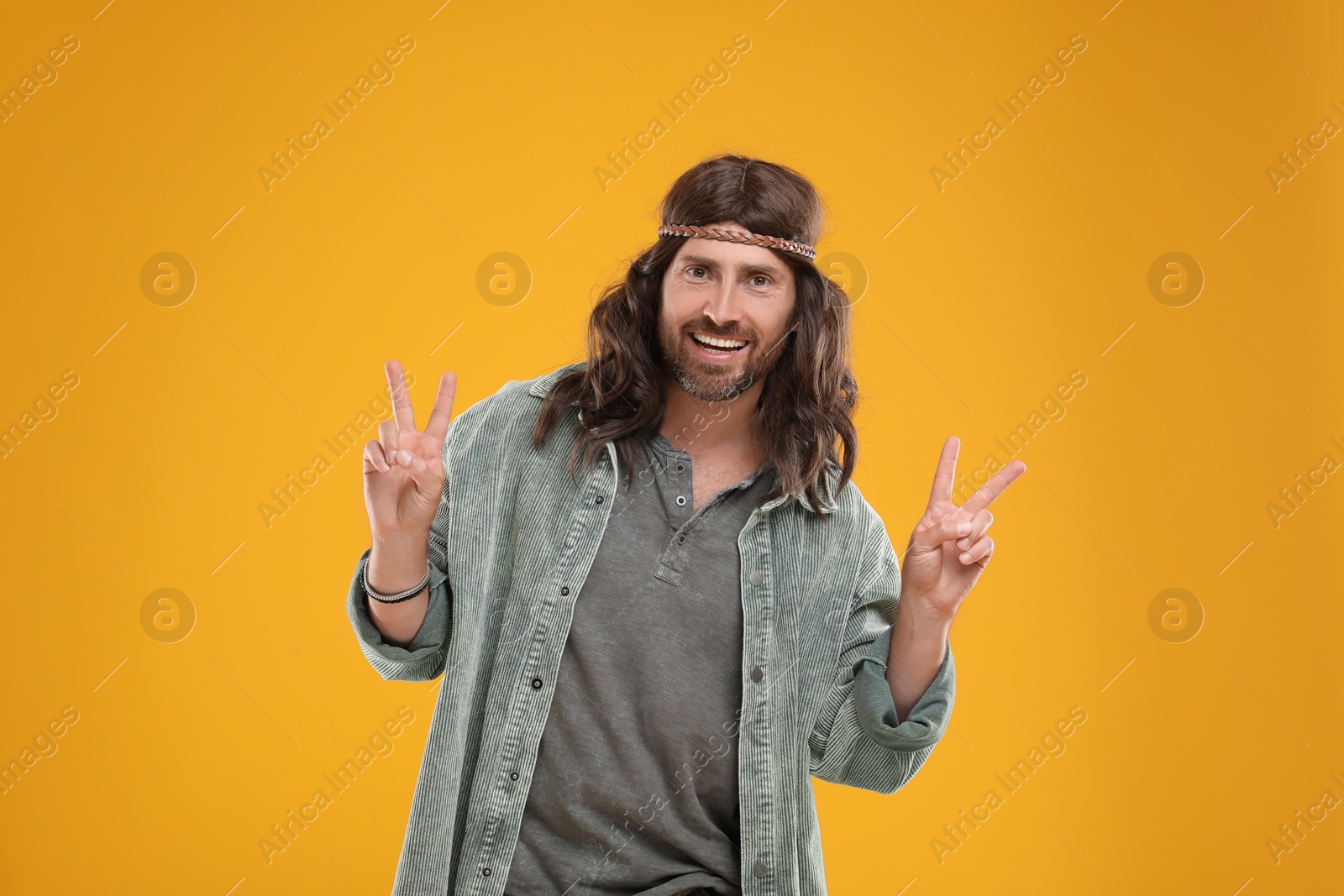 Photo of Stylish hippie man showing V-sign on orange background