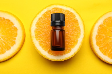 Bottle of citrus essential oil and fresh orange on yellow background, flat lay