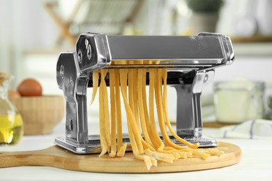 Photo of Pasta maker with raw dough on white wooden table, closeup