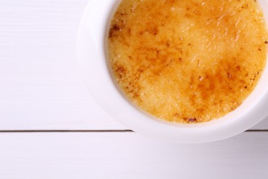 Photo of Delicious creme brulee in bowl on white wooden table, top view. Space for text