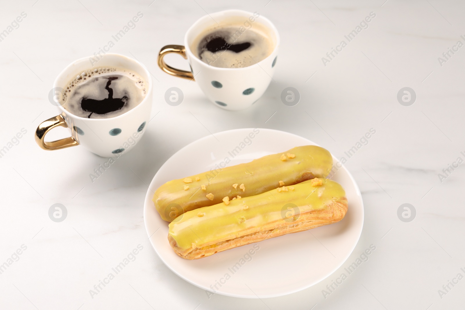 Photo of Tasty glazed eclairs and cups of coffee on white marble table, closeup