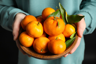 Woman holding bowl of tangerines, closeup. Juicy citrus fruit