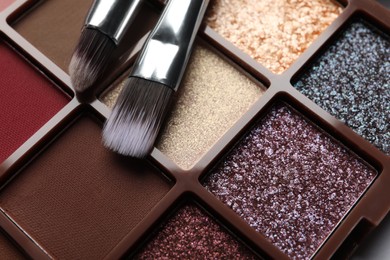 Photo of Beautiful eye shadow palette and brushes on table, closeup