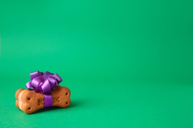 Photo of Bone shaped dog cookies with purple bow on green background. Space for text