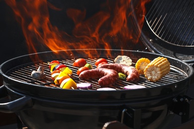 Photo of Tasty sausages and vegetables on burning barbecue grill