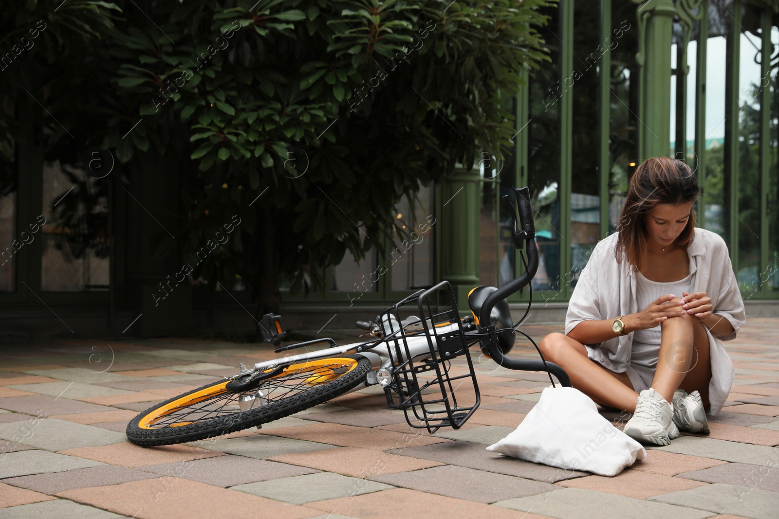 Photo of Young woman with injured knee near bicycle on city street. Space for text