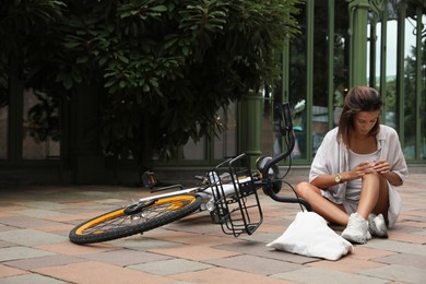 Young woman with injured knee near bicycle on city street. Space for text