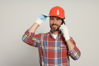 Professional builder in hard hat talking on phone against light background