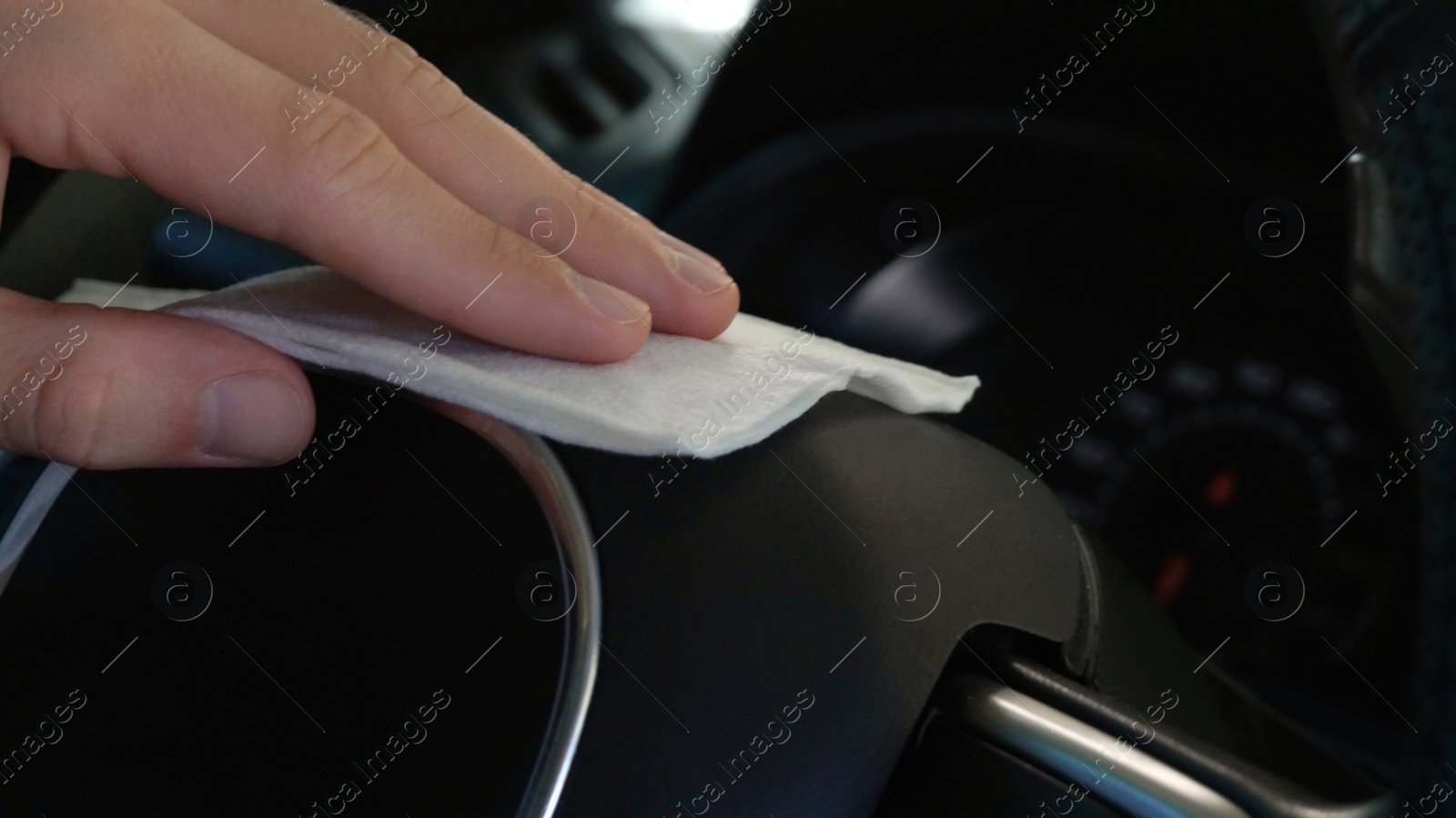 Photo of Man cleaning steering wheel with wet wipe in car, closeup. Protective measures