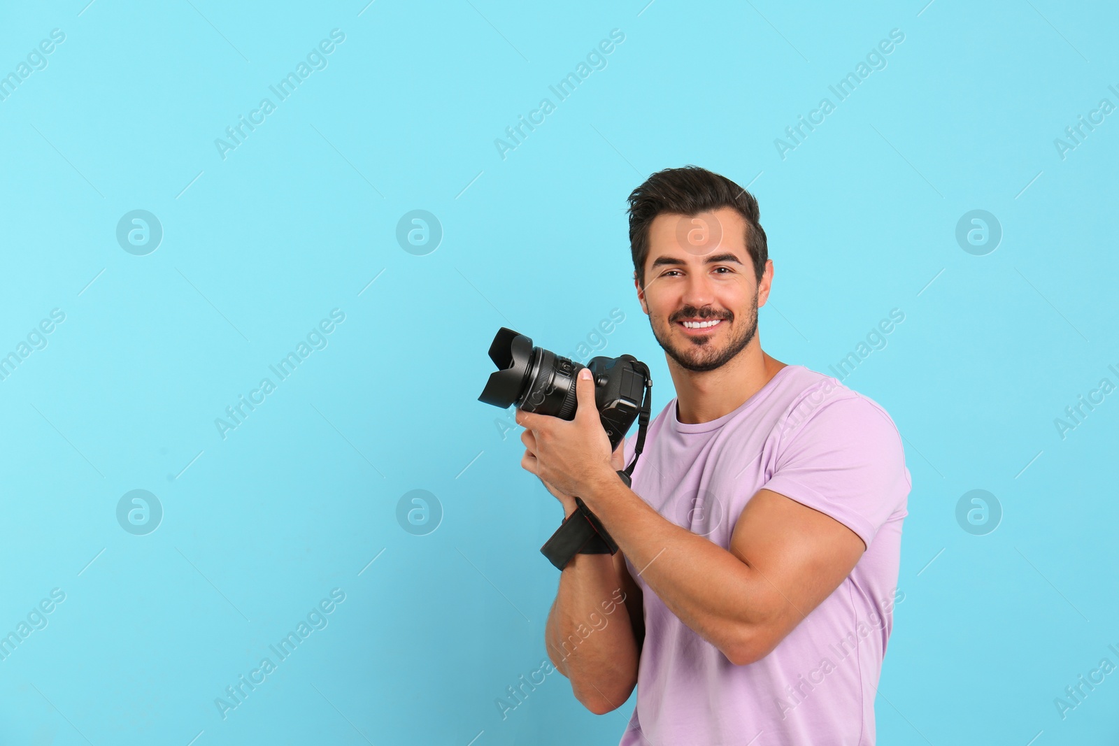 Photo of Young photographer with professional camera on light blue background. Space for text