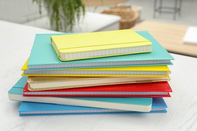 Photo of Stack of colorful planners on white wooden table indoors