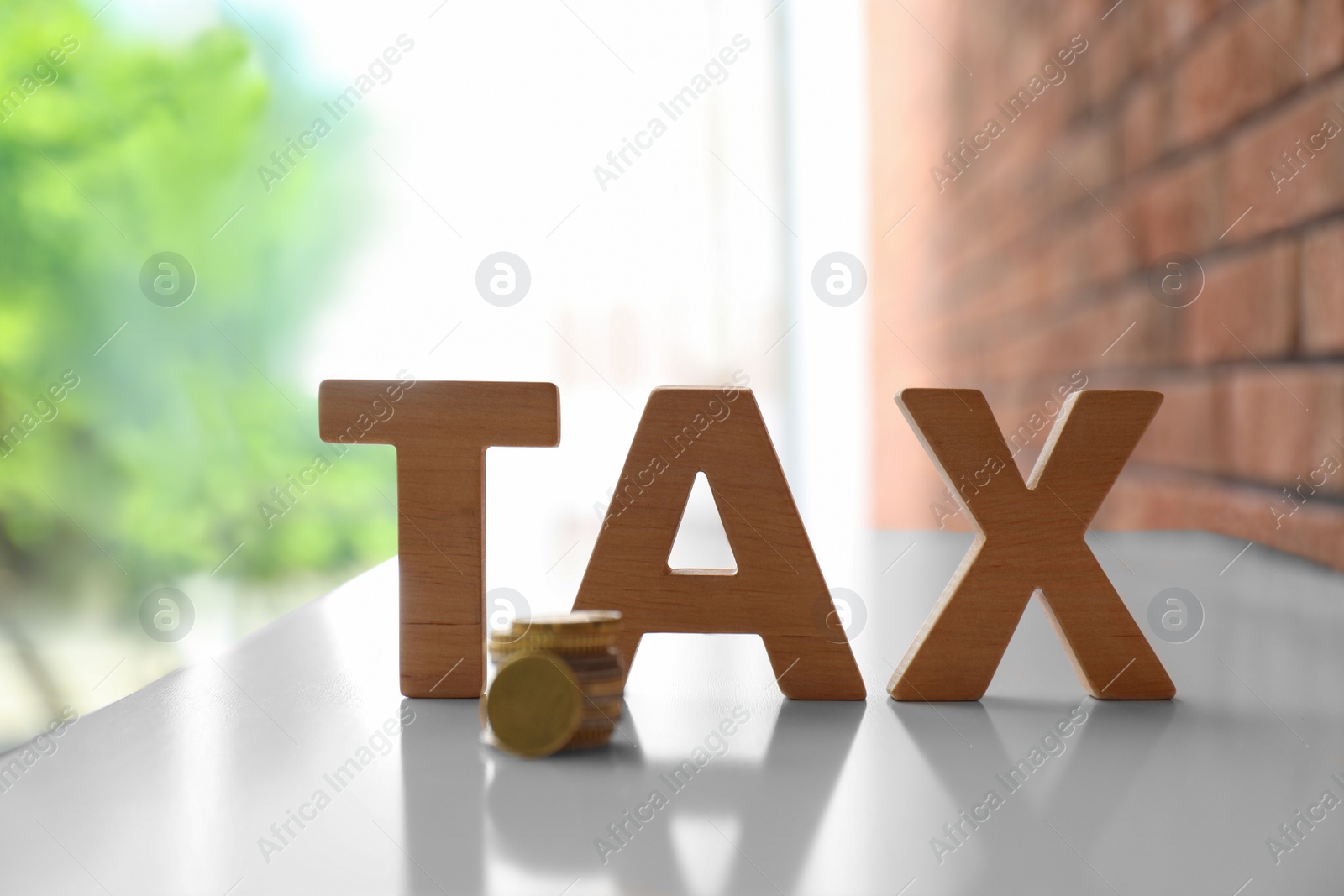 Photo of Word TAX made of letters and coins on table against blurred background
