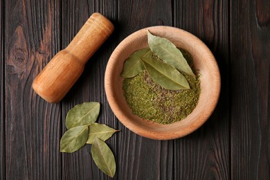 Photo of Mortar, pestle with whole and ground aromatic bay leaves on wooden table, flat lay