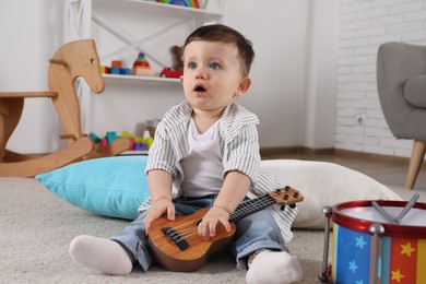 Photo of Cute little boy with toy guitar at home