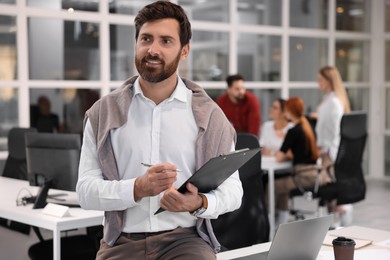 Photo of Team of employees working together in office. Happy man with clipboard indoors