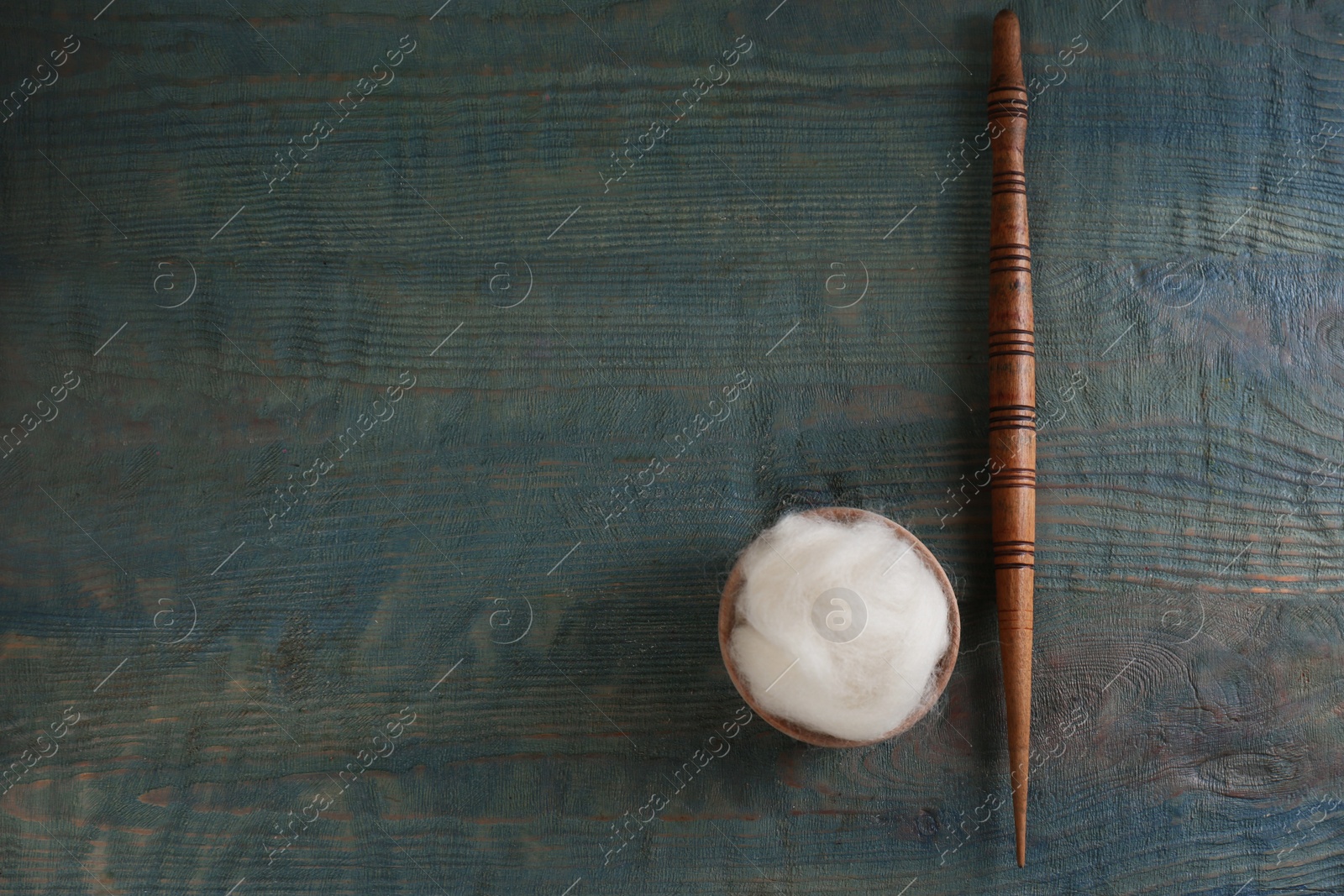 Photo of Soft white wool and spindle on blue wooden table, flat lay. Space for text