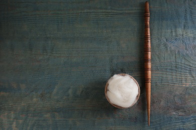 Soft white wool and spindle on blue wooden table, flat lay. Space for text