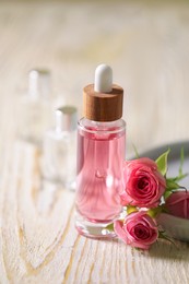 Photo of Bottle of essential rose oil and flowers on white wooden table