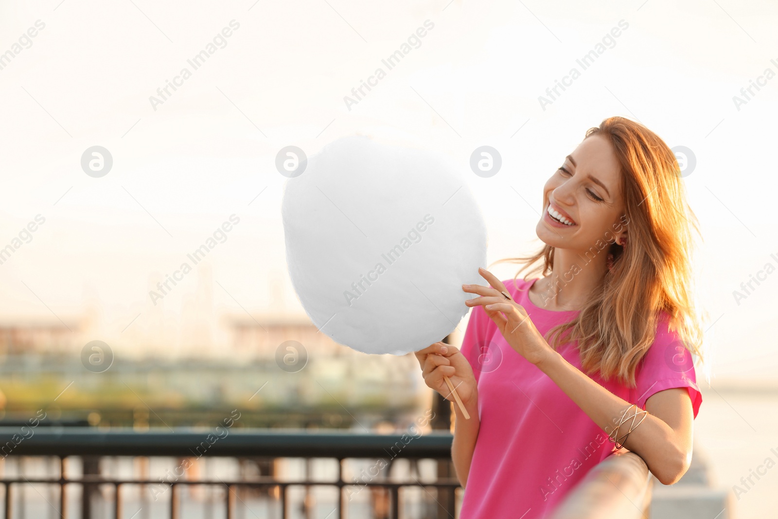 Photo of Happy young woman with cotton candy on waterfront. Space for text