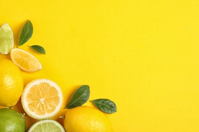 Fresh ripe lemons, limes and green leaves on yellow background, flat lay. Space for text