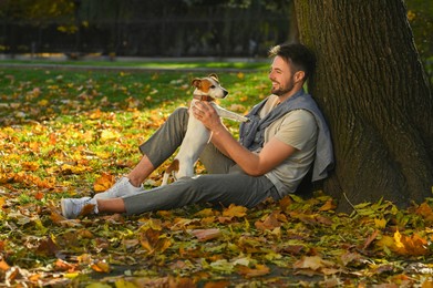 Photo of Man with adorable Jack Russell Terrier in autumn park, space for text. Dog walking