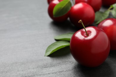 Delicious ripe cherry plums with leaves on black table, closeup. Space for text