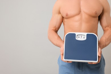Photo of Athletic man holding scales on light grey background, closeup and space for text. Weight loss concept