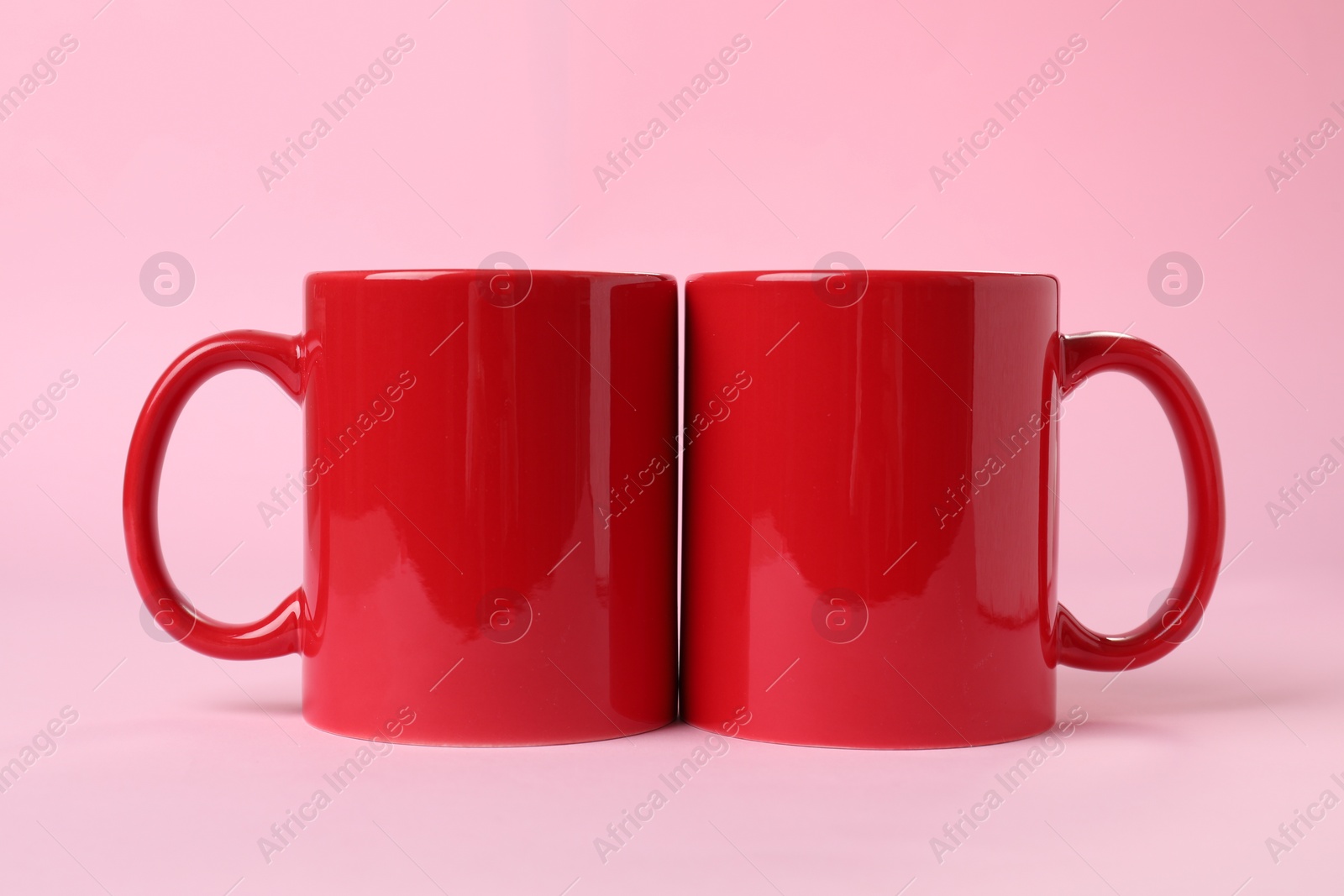 Photo of Two red ceramic mugs on pink background