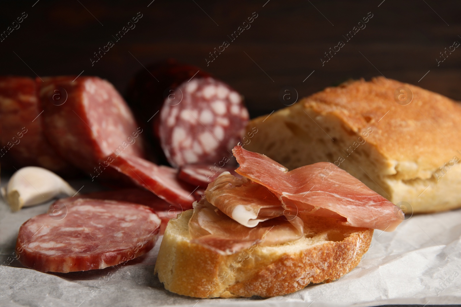 Photo of Delicious bread with prosciutto and other sausages on parchment paper, closeup