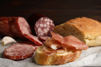 Photo of Delicious bread with prosciutto and other sausages on parchment paper, closeup