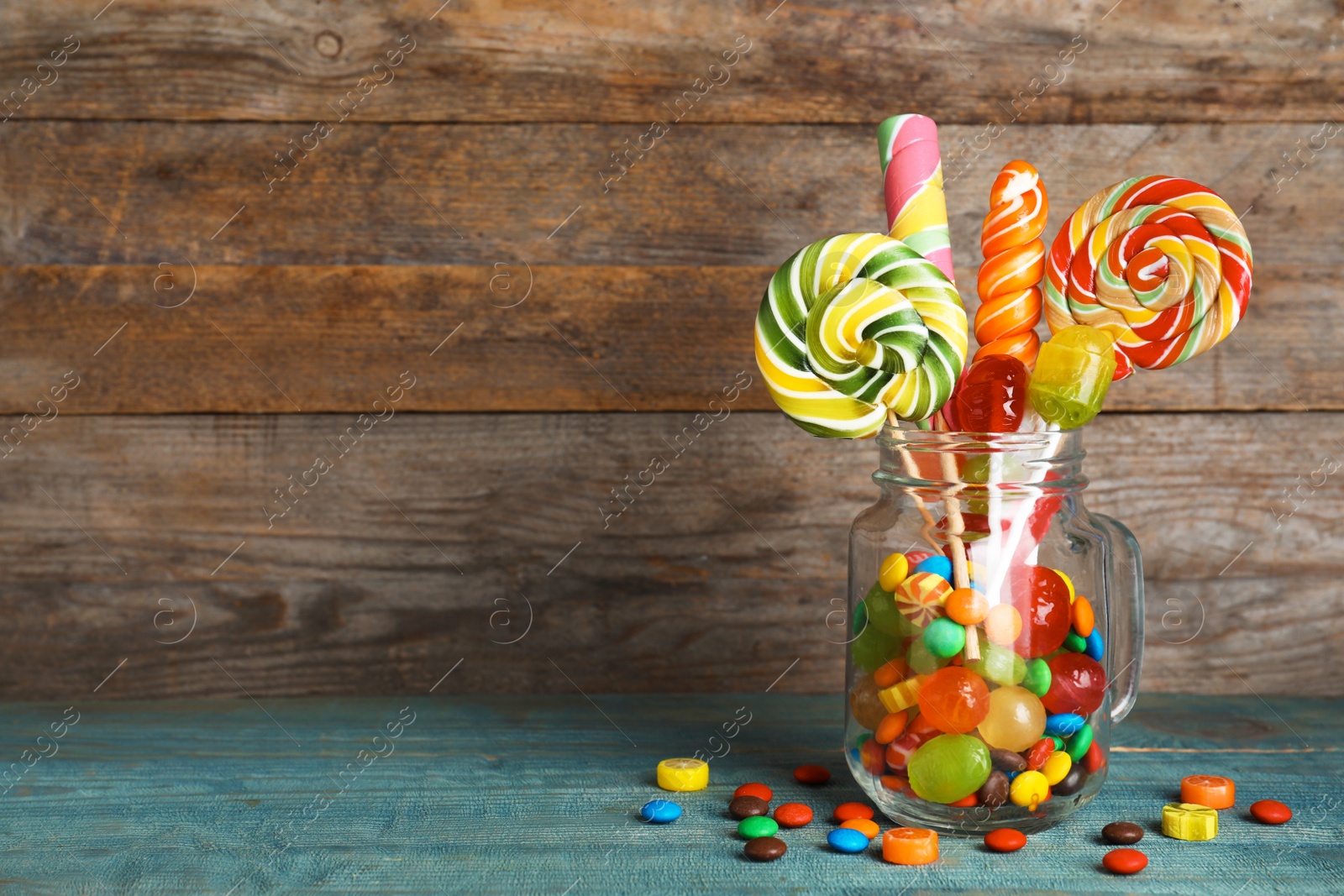 Photo of Mason jar with different colorful candies on wooden background. Space for text