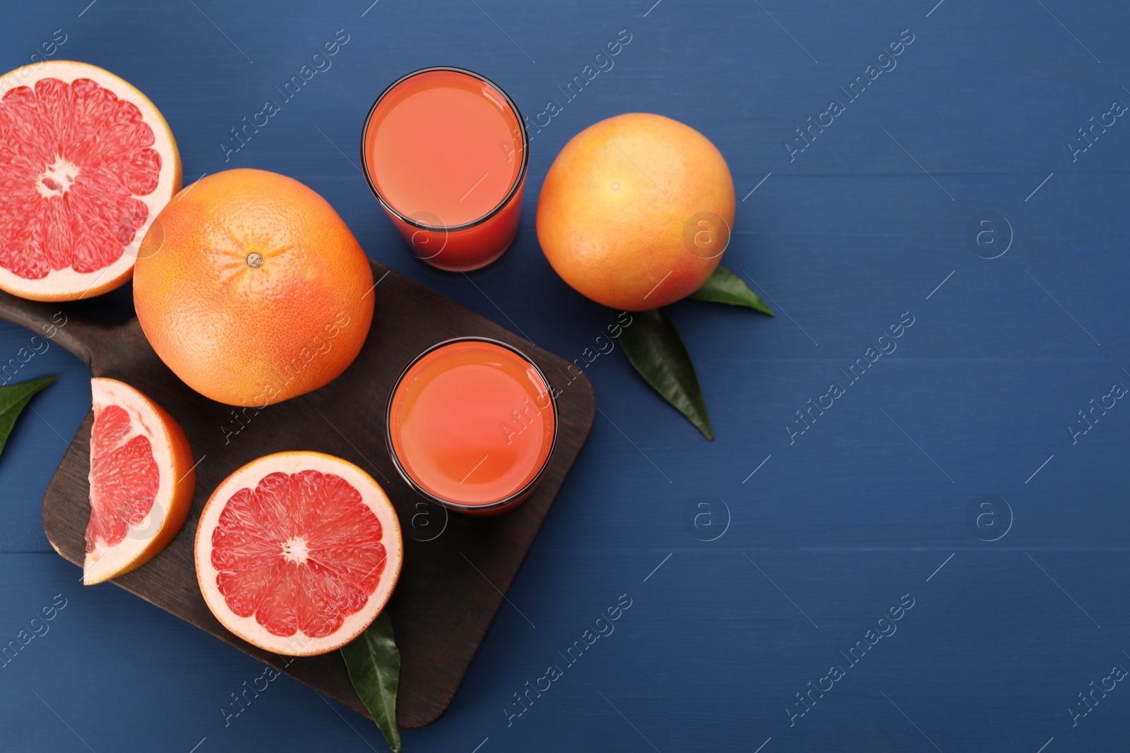 Photo of Tasty grapefruit juice in glasses and fresh fruits on blue wooden table, flat lay. Space for text