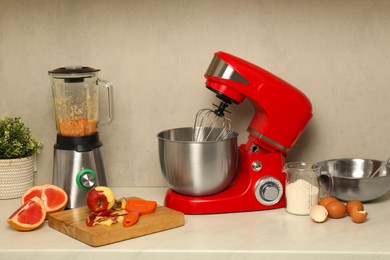 Photo of Modern red stand mixer, blender and different ingredients on white marble table