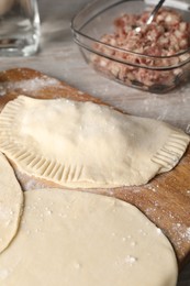 Raw chebureki with tasty filling on wooden table, closeup