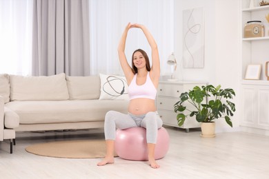 Pregnant woman doing exercises on fitness ball in room. Home yoga