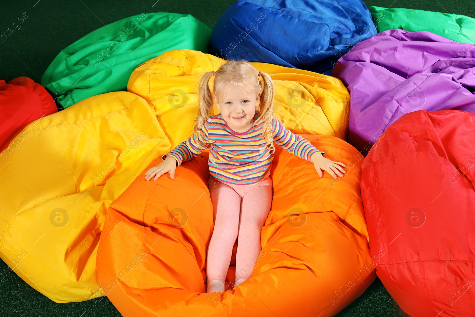 Photo of Cute child playing on colorful bean bag chairs indoors