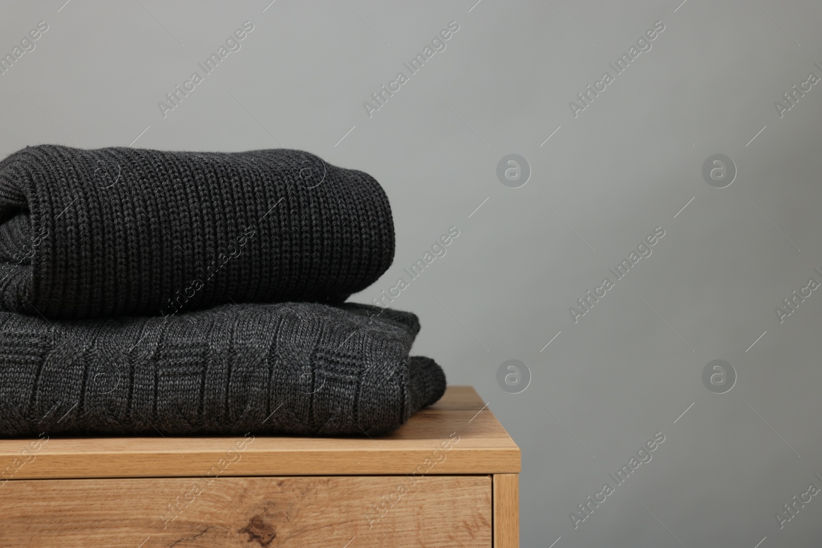 Photo of Stack of knitted sweaters on wooden table against grey background. Space for text