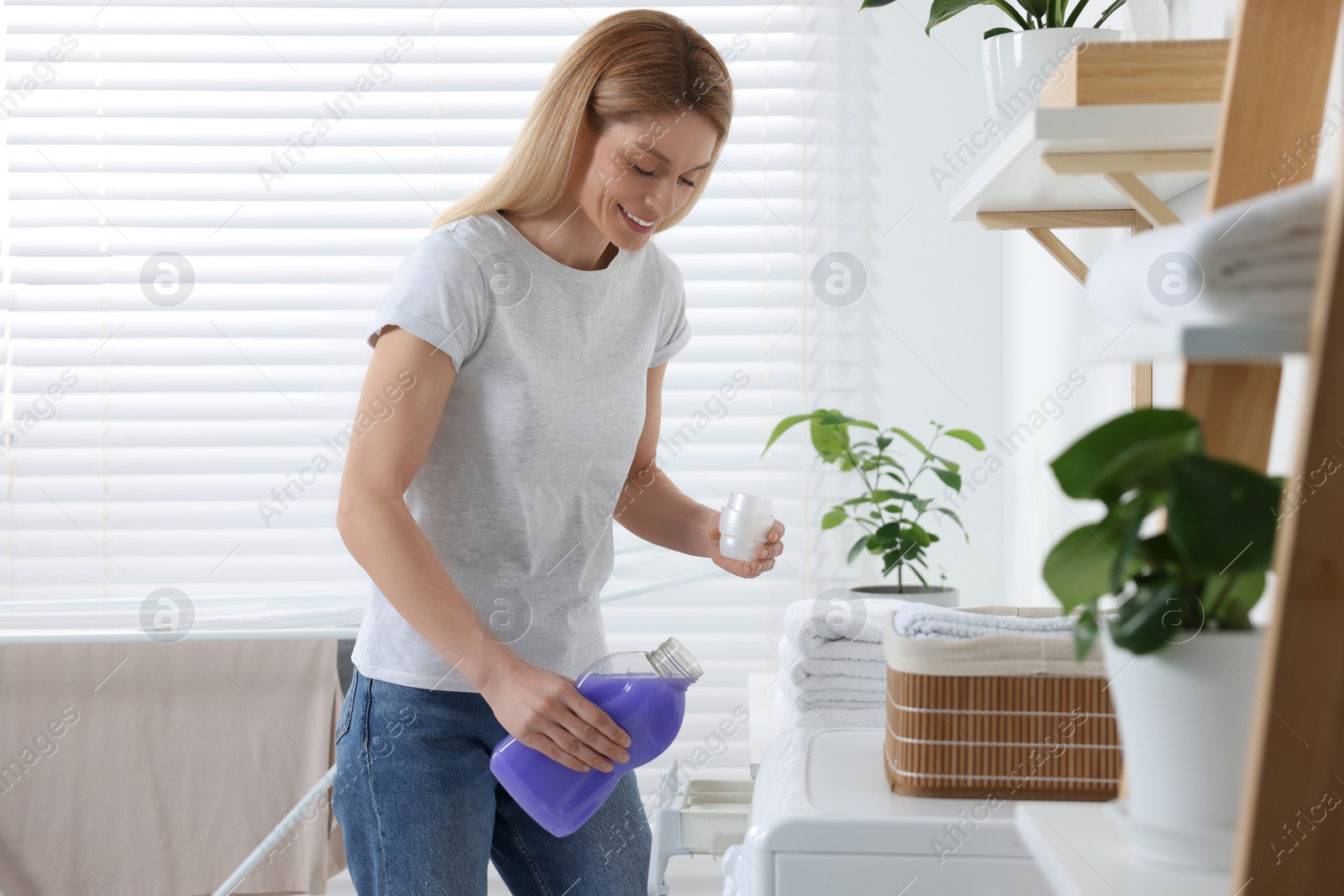 Photo of Woman pouring fabric softener into washing machine in bathroom