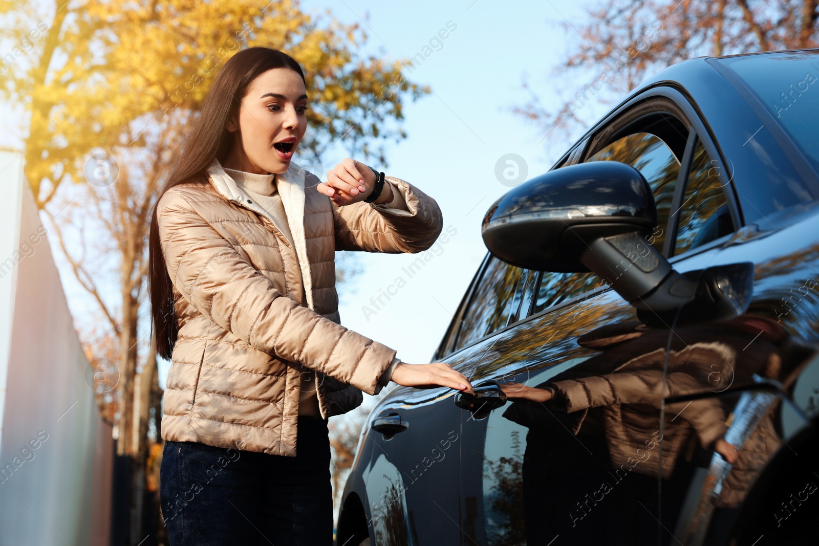 Photo of Emotional woman checking time on watch near car. Being late concept