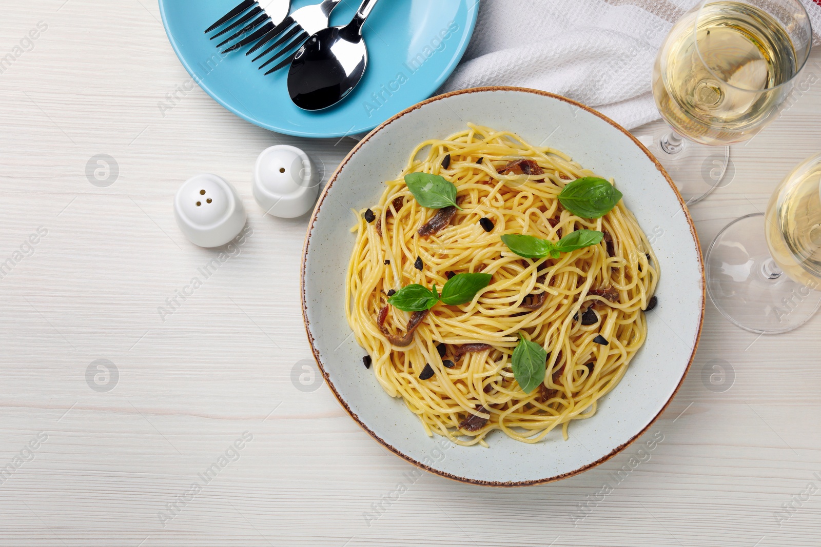 Photo of Delicious pasta with anchovies, glasses of drink and cutlery on white wooden table, flat lay. Space for text