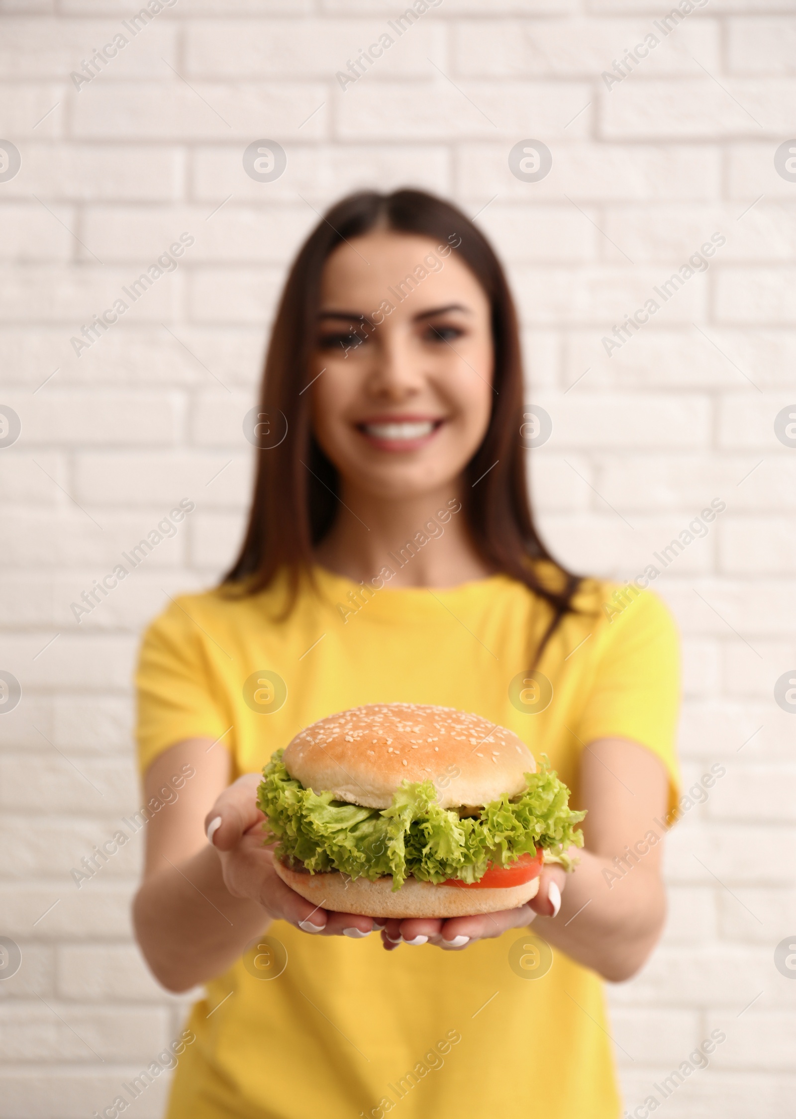 Photo of Young woman with tasty burger near brick wall