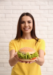 Young woman with tasty burger near brick wall