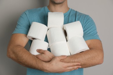 Photo of Man with heap of toilet paper rolls on grey background, closeup